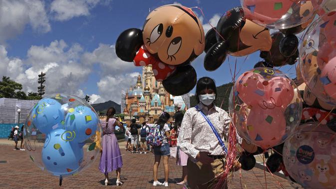 Pegawai yang mengenakan masker untuk mencegah penyebaran COVID-19 menjual balon di Disneyland Hong Kong, Kamis (18/6/2020). Disneyland Hong Kong kembali beroperasi pada 18 Juni 2020 dengan menerapkan sejumlah protokol kesehatan baru. (AP Photo/Kin Cheung)