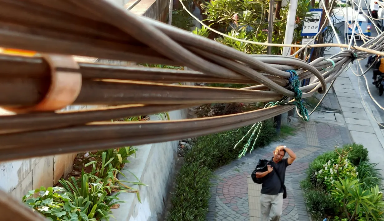Pejalan kaki melintas di bawah kabel semrawut di sekitar Jalan Gunung Sahari, Mangga Dua, Jakarta, Kamis (10/7/2019). Buruknya tata instalasi kabel di Ibu Kota menjadi penyebab banyaknya kabel semrawut, meskipun kondisi itu berbahaya serta mengganggu pemandangan. (Liputan6.com/Immanuel Antonius)