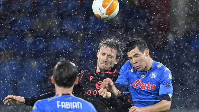 Bek Real Sociedad, Nacho Monreal (tengah) dan penyerang Napoli, Hirving Lozano (kanan) melakukan sundulan pada matchday terakhir Grup F Liga Europa di Diego Armando Maradona, Jumat (11/12/2020) dini hari WIB. Napoli bermain imbang 1-1 melawan Real Sociedad. (Alberto PIZZOLI / AFP)