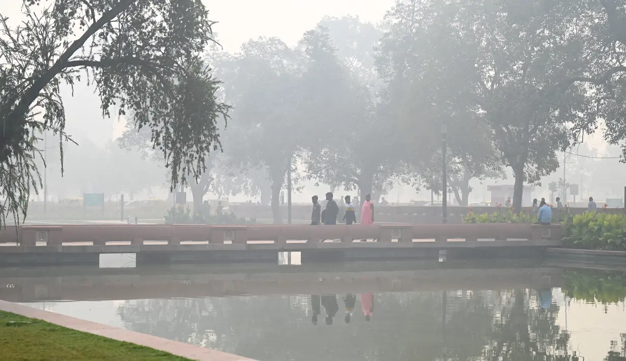 Pejalan kaki berjalan di sepanjang jalan dekat Gerbang India di tengah kabut asap tebal di New Delhi, Kamis (3/11/2022). Jarak pandang pun berkurang di kota berpenduduk 20 juta orang tersebut. (Photo by Money SHARMA / AFP)
