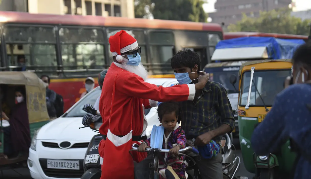 Aksi presiden Angel Foundation dan pekerja sosial, Rufas Christian, yang berpakaian Sinterklas memakaikan masker kepada pengguna jalan di persimpangan lalu lintas di Ahmedabad, India, Kamis (17/12/2020). India sejauh ini telah mencatat hampir 10 juta kasus Covid-19. (SAM PANTHAKY / AFP)