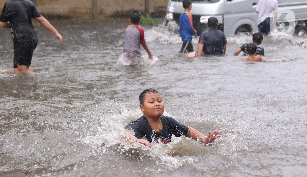 Sejumlah anak bermain banjir saat melanda jalan Bayangkara Pusdiklat, Kota Tangerang Selatan, Banten, Selasa (2/11/2021). Aksi anak anak tersebut dapat membahayakan keselamatan jiwa karena banyaknya kendaraan yang melintas menerjang banjir. (Liputan6.com/Angga Yuniar)