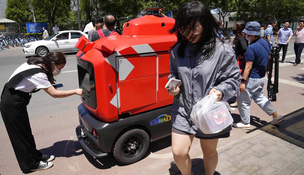 Pekerja mengambil pesanan mereka dari kendaraan pengiriman otonom yang dioperasikan oleh JD.com di jalanan Beijing, China, Jumat (28/5/2021). Raksasa e-commerce China JD.com meningkatkan operasi kendaraan pengiriman tak berawak. (AP Photo/Ng Han Guan)