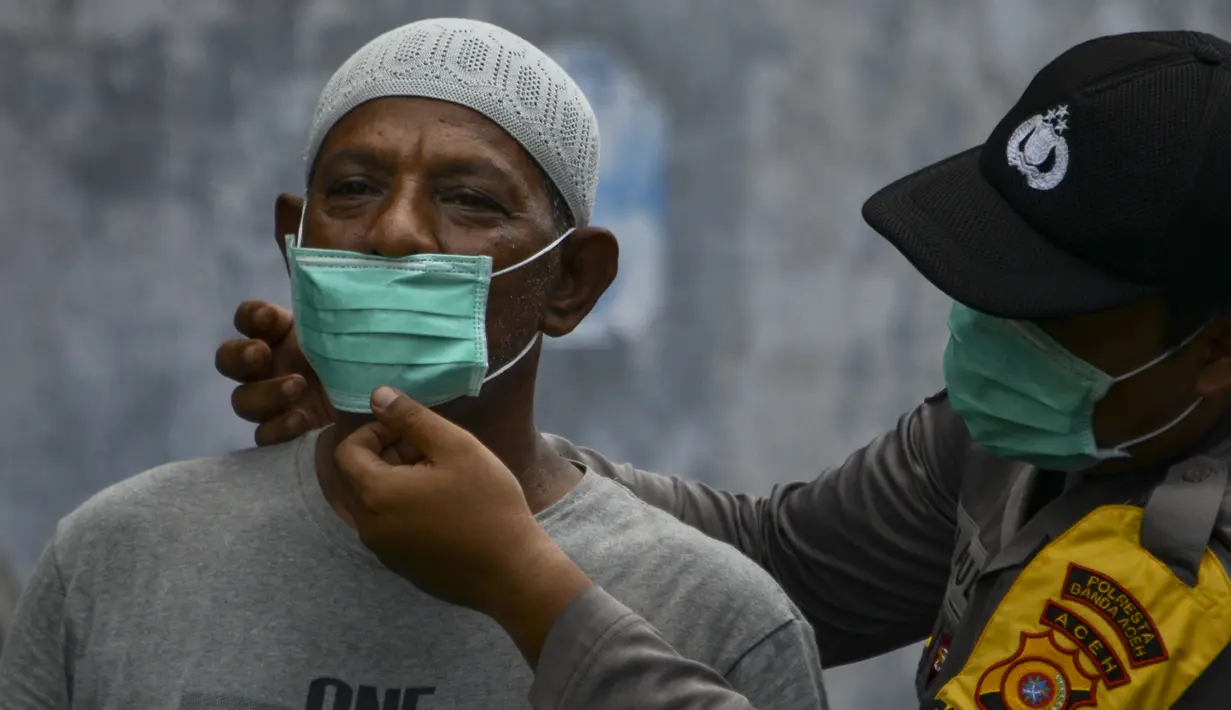 Petugas polisi memasangkan masker kepada warga saat kabut asap tebal menyelimuti wilayah Banda Aceh (25/9/2019). Kebakaran hutan Indonesia menyebabkan hampir 10 juta anak dalam risiko pencemaran udara. (AFP Photo/Chaideer Mahyuddin)