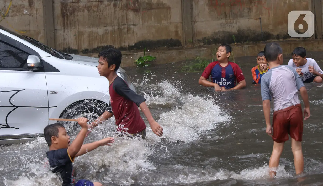 Sejumlah anak bermain banjir saat melanda jalan Bayangkara Pusdiklat, Kota Tangerang Selatan, Banten, Selasa (2/11/2021). Aksi anak anak tersebut dapat membahayakan keselamatan jiwa karena banyaknya kendaraan yang melintas menerjang banjir. (Liputan6.com/Angga Yuniar)
