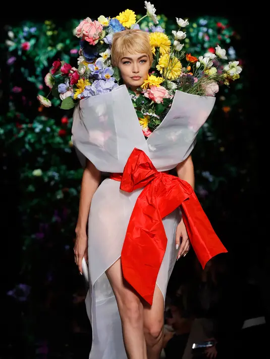 Gigi Hadid tampil dengan busana koleksi rumah mode Moschino saat Milan Fashion Week di Italia, Kamis (21/9). Gigi Hadid terlihat seperti buket bunga dengan hiasan bunga dikepala dan balutan pita merah dibagian pinggangnya. (AP Photo/Luca Bruno)