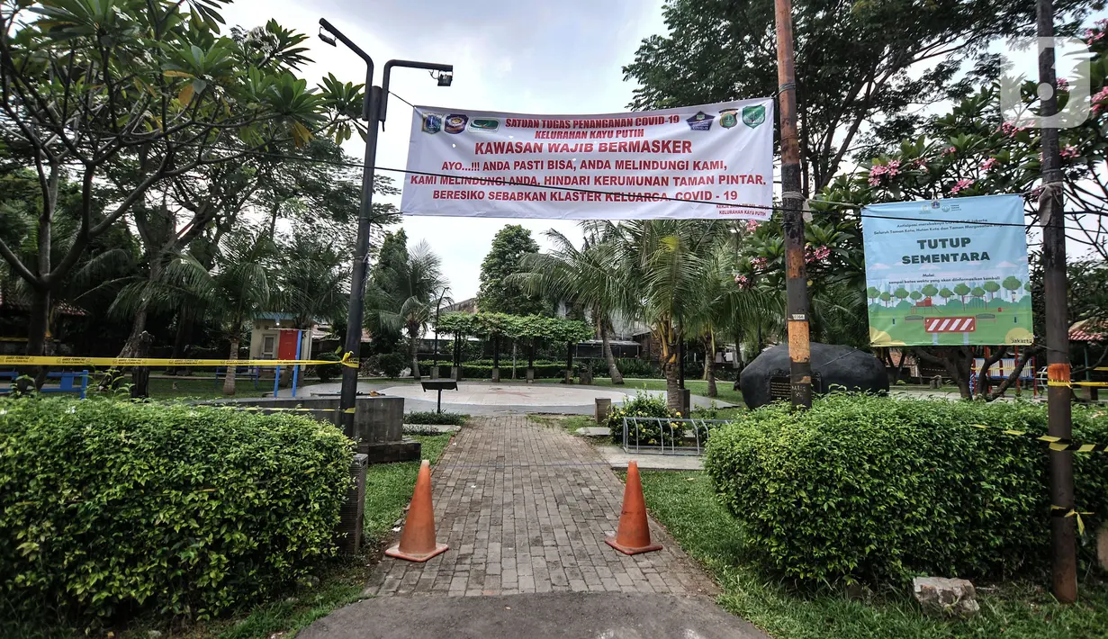 Spanduk terpasang di taman saat pemberlakuan karantina wilayah skala kecil atau mini lockdown di RT 011 RW 009, Kelurahan Kayu Putih, Pulogadung, Jakarta Timur, Minggu (6/6/2021). Sebanyak 14 warga positif COVID-19 saat ini telah dibawa ke RSD Wisma Atlet Kemayoran. (merdeka.com/Iqbal S. Nugroho)