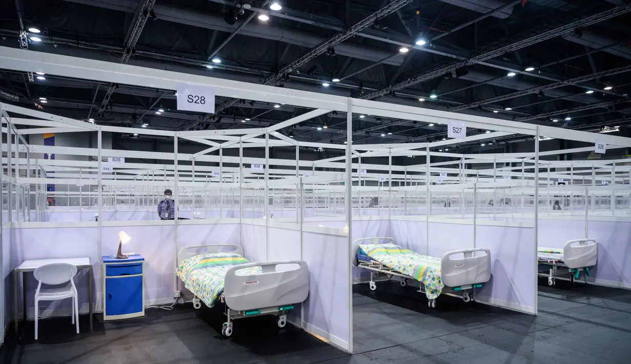 Petugas keamanan (kiri) berjaga di samping deretan kamar yang dipartisi di fasilitas perawatan kesehatan masyarakat di AsiaWorld-Expo di Hong Kong, Selasa (24/11/2020). Rumah sakit darurat khusus corona itu kembali dibuka menyusul lonjakan kasus COVID-19 di Hong Kong. (Anthony WALLACE/AFP)