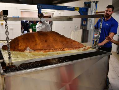 Koki dan relawan Muslim Aid menimbang berat makanan ringan berbentuk segitiga, samosa raksasa, di Masjid London Timur, London, Inggris, Selasa (22/8). Samosa berukuran raksasa seberat 153 kilogram itu menjadi yang terbesar di dunia. (BEN STANSALL/AFP)