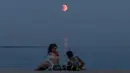 Fenomena ini merupakan gerhana bulan total kedua yang berlangsung sepanjang tahun 2025. Tampak dalam foto, para pengunjung pantai beristirahat di tepi pantai Laut Hitam dengan bulan purnama yang juga dikenal sebagai “Blood Moon” selama fase gerhana bulan total di latar belakang di Odesa, Ukraina pada 7 September 2025. (Oleksandr GIMANOV/AFP)
