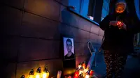 Seorang wanita menyalakan lilin di dekat foto Jan Kuciak di Bratislava (26/2). Pembunuhan itu terjadi di tengah pembuatan laporan investigatif Kuciak soal kasus dugaan kecurangan pajak yang melibatkan pengusaha. (AFP Photo/Vladimir Simicek)