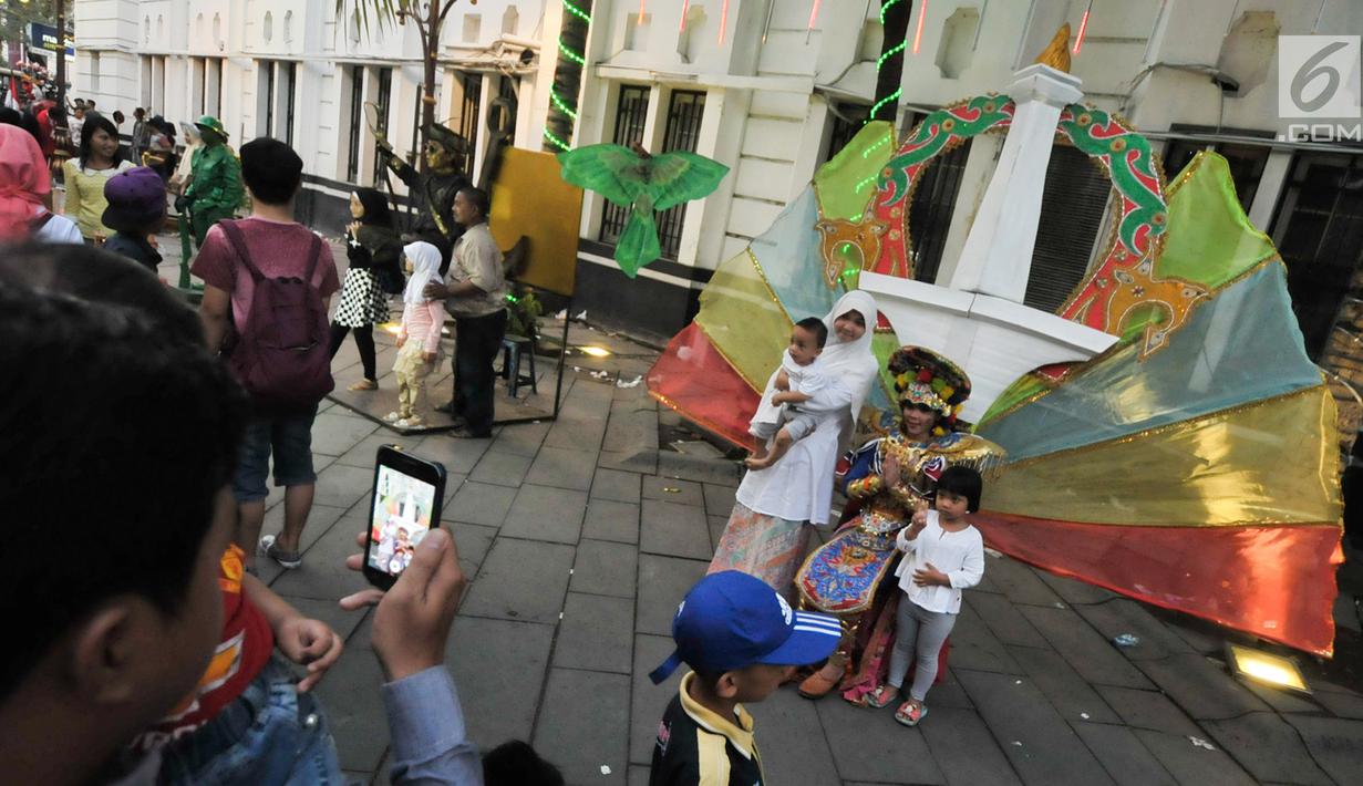 Pengunjung berfoto dengan manusia patung dan berkostum di kawasan Kota Tua, Jakarta, Selasa (27/6). Mereka mengajak sanak keluarga untuk menghabiskan waktu berlibur Lebaran 2017. (Liputan6.com/Yoppy Renato)