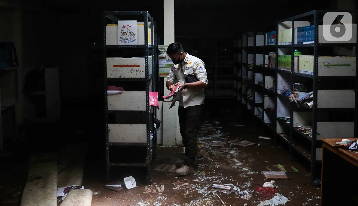 Petugas memeriksa berkas-berkas saat membersihkan ruangan di MTsN 19 Pondok Labu, Jakarta, Jumat (7/10/2022). Petugas PPSU, Satpol PP, dan Dinas Pemadam Kebakaran membersihkan ruang kelas, kantin, dan fasilitas lainnya usai terendam banjir pada Kamis sore kemarin. (Liputan6.com/Herman Zakharia)