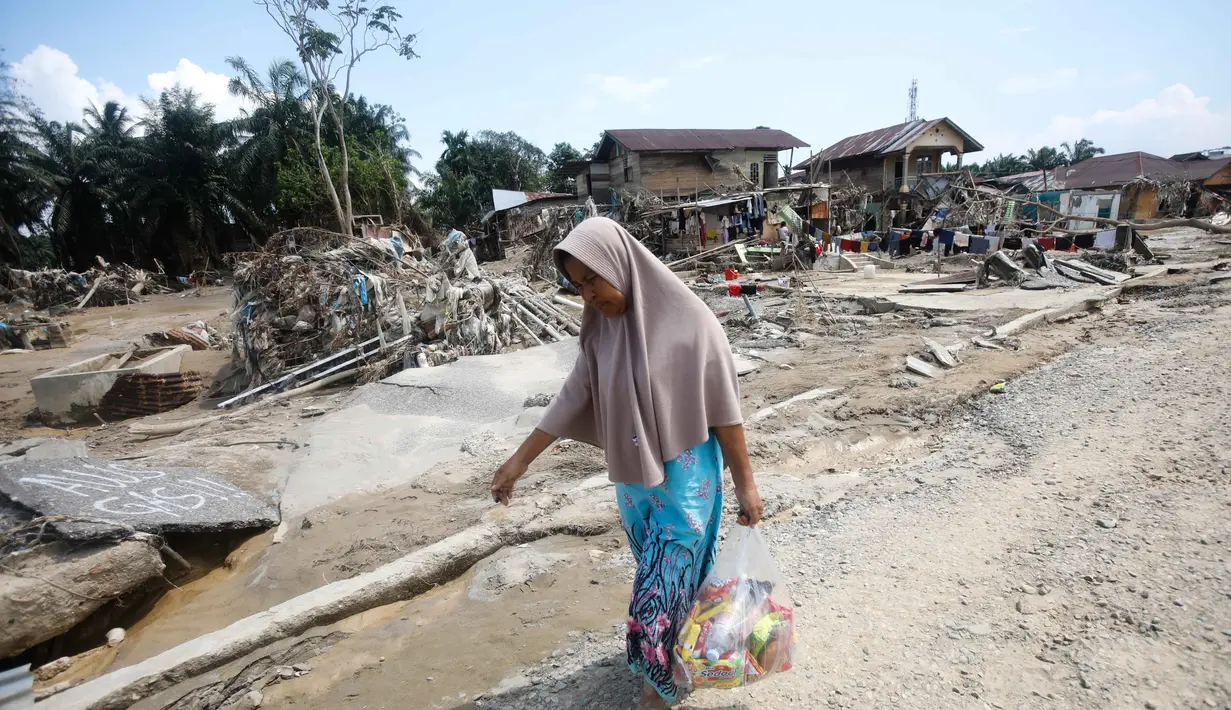 Sejumlah kendaraan roda empat teronggok dengan posisi terbalik atau tercebur ke parit. Tampak dalam foto, seorang korban membawa barang-barang bantuan di daerah yang terdampak banjir bandang di Aceh Tamiang, Sumatera, Indonesia, Jumat 5 Desember 2025. (AP Photo/Binsar Bakkara)