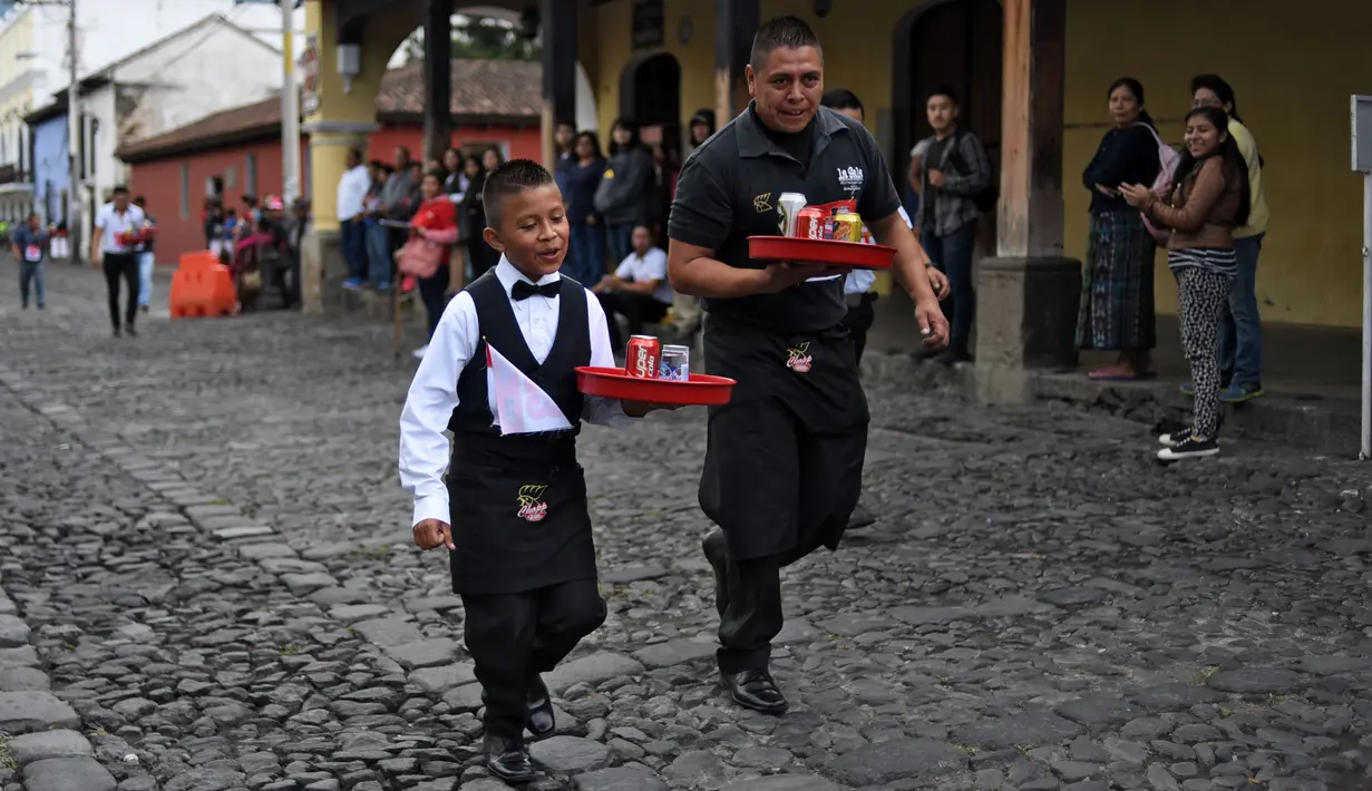 Pramusaji dan seorang anak beradu kecepatan sambil membawa nampan dalam Waiters Race ke-16 di Antigua, barat daya Ibu Kota Guatemala City, Rabu (14/11). Lomba ini diikuti oleh ratusan peserta yang merupakan pelayan restoran dan kafe. (JOHAN ORDONEZ/AFP)