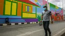 Seorang warga melintasi mural yang tengah dibuat di Flyover Gaplek, Tangerang Selatan, Rabu (10/3/2021). Dengan mengangkat budaya lokal, simbol-simbol Betawi digambar menggunakan 1.200 Liter cat beragam warna. dan mural ditargetkan rampung pada akhir Maret 2021. (Liputan6.com/Faizal Fanani)