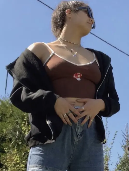 <p>spaghetti tank top cokelat dengan gambar jamur yang dipadukan outer jaket hitam crop top juga menjadi penampilan Masniari. Dikombinasikan dengan celana denim dan berbagai aksesori yang ia kenakan.&nbsp;@masiwolf</p>