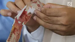 Karyawan memegang uang kertas 100 ribu rupiah di tempat penukaran uang rusak di Gedung Bank Indonessia, Jakarta (4/4). Adapun syarat penukaran uang rusak adalah minimal 2/3 bagian uang masih utuh dan masih ada nomor seri. (Merdeka.com/Arie Basuki)