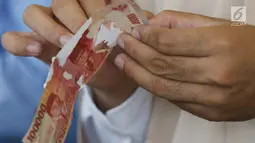 Karyawan memegang uang kertas 100 ribu rupiah di tempat penukaran uang rusak di Gedung Bank Indonessia, Jakarta (4/4). Adapun syarat penukaran uang rusak adalah minimal 2/3 bagian uang masih utuh dan masih ada nomor seri. (Merdeka.com/Arie Basuki)