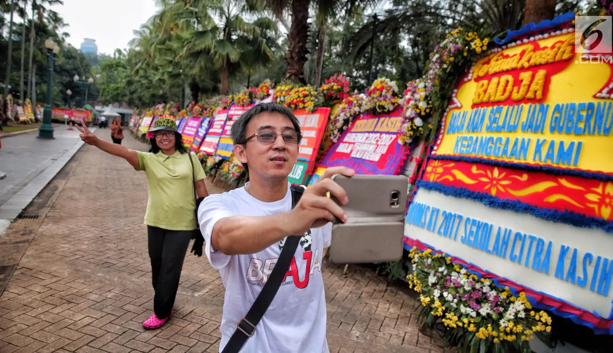 Warga berselfie di dekat karangan bunga di Balai Kota DKI Jakarta, Kamis (12/10). Anies Baswedan dan Sandiaga Uno akan menjadi gubernur DKI Jakarta untuk periode jabatan 2017-2022. (Liputan6.com/Faizal Fanani)