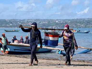 Para pekerja membawa ikan setelah para nelayan menurunkan hasil tangkapan mereka dari perahu di pantai Kedonganan dekat Denpasar, Bali, pada Jumat 10 April 2026. Provinsi Bali memiliki sejumlah pelabuhan yang berperan penting dalam mendukung kegiatan perikanan dan kelautan. (SONNY TUMBELAKA/AFP)