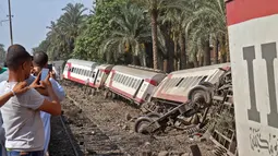 Sejumlah warga mengabadikan gerbong kereta usai tergelincir saat melintasi jalur di daerah al-Badrasheen, Giza, Mesir, (13/7). Dalam kejadian tersebut, tidak ada korban jiwa dan sekitar 55 penumpang terluka. (AFP Photo/Stringer)