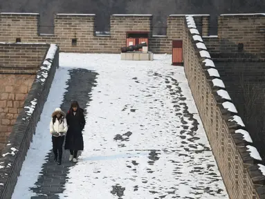 Dua wisatawan berjalan usai hujan salju mengguyur Tembok Besar China di utara Beijing (6/1/2020). Awal tahun 2020, musim dingin turun menyelimuti bagian utara Beijing yang mengakibatkan lokasi wisata yang menjadi salah satu keajaiban dunia tertutup salju. (AFP/Greg Baker)