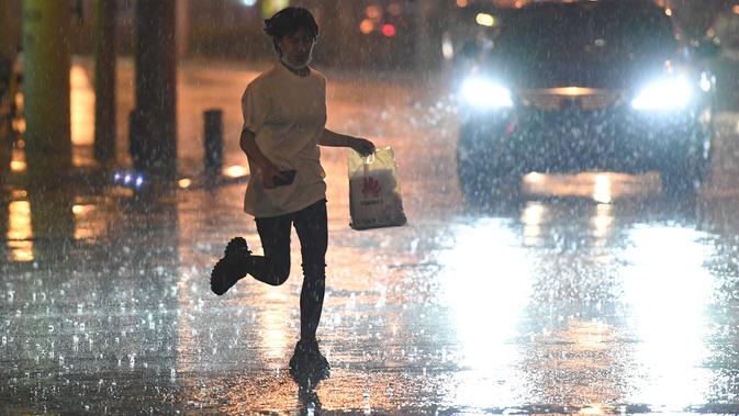 Seorang wanita berlari di bawah guyuran hujan di Distrik Chaoyang, Beijing, China (12/8/2020). Badan meteorologi Beijing mengeluarkan peringatan siaga kuning untuk hujan badai. (Xinhua/Ju Huanzong)