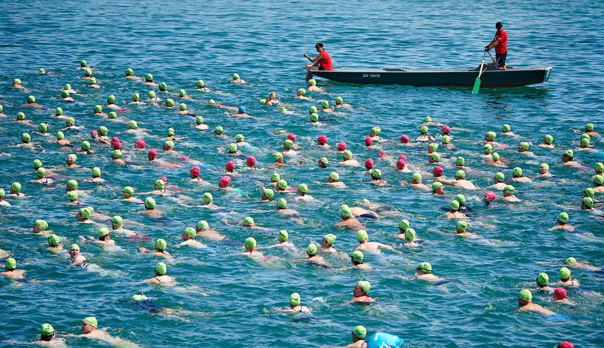 Dua orang di atas perahu mengawasi para peserta dalam perhelatan tahunan menyeberangi Danau Zurich di Swiss, 5 Juli 2017. Dalam ajang tersebut, ratusan peserta harus bersaing mengarungi Danau Zurich sejauh 1,5 kilometer. (AFP PHOTO / Michael Buholzer)