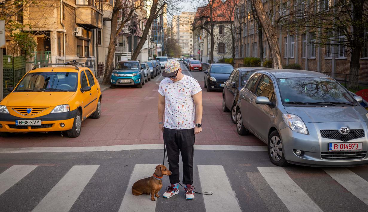 Alexandru Tigoianu (36) berpose dengan anjingnya Tix (3) di Bucharest (29/3/2020). Undang-undang militer, yang disahkan pemerintah Rumania untuk mengurangi penyebaran virus corona, menyatakan berjalan bersama anjing adalah salah satu  kegiatan yang masih diizinkan. (AFP/Andrei Pungovschi)