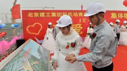 Pengantin pria memperlihatkan rancangan bandara pada pengantin wanitanya, Beijing, Senin (12/12). Kelima pekerja ini kompak untuk menggelar upacara pernikahan di tempat proyek mereka bekerja yaitu sebuah bandara. (AFP PHOTO)