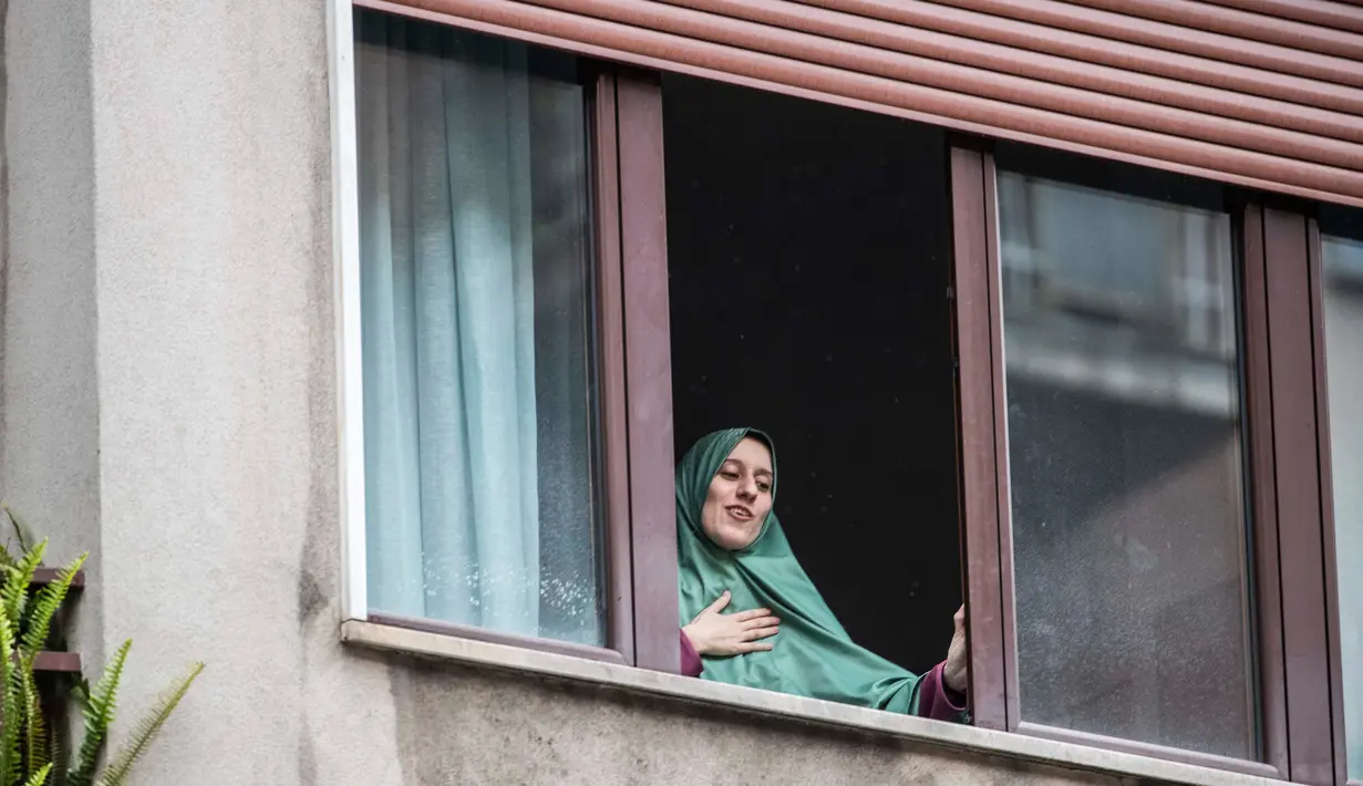 Petugas bantuan Italia Silvia Romano, yang dibebaskan oleh militan Somalia, terlihat di jendela setelah tiba di rumahnya di Milan, 11 Mei 2020. Terkait keputusan menjadi mualaf, Silvia dengan tegas mengatakan telah bersyahadat selama penculikan dan itu pilihannya tanpa paksaan. (AP/Luca Bruno)