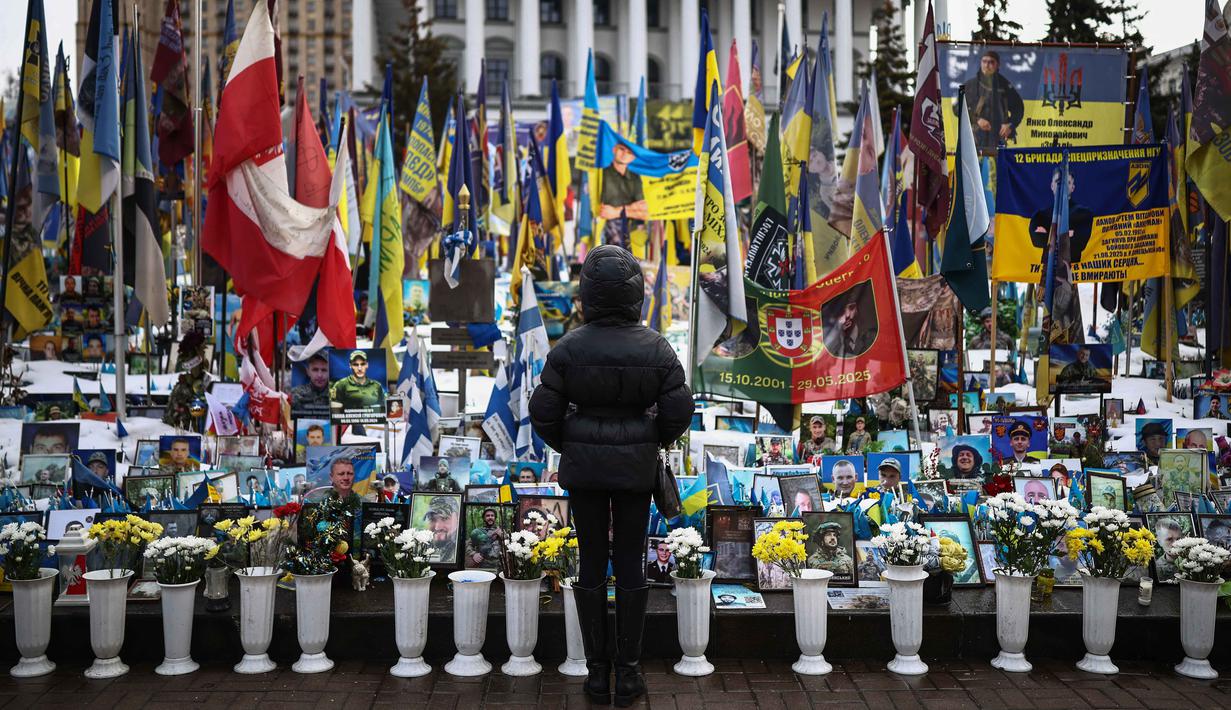 Seorang warga setempat berdiri di depan tugu peringatan sementara untuk tentara Ukraina di Lapangan Kemerdekaan, Kyiv, saat peringatan keempat invasi Rusia ke Ukraina, Selasa 24 Februari 2026. Hari ini, perang Rusia-Ukraina yang pecah pada 24 Februari 2022 telah berlangsung selama empat tahun. (HENRY NICHOLLS/AFP)