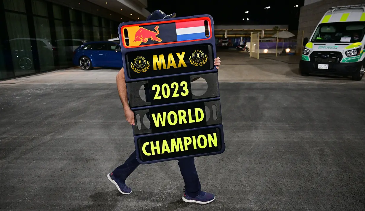 Seorang kru tim Red Bull Racing membawa papan bertuliskan Max Verstappen sebagai juara dunia Formula 1 2023 setelah Sprint Race F1 GP Qatar 2023 yang dihelat di Sirkuit Lusail, Qatar, Minggu (8/10/2023) dini hari WIB. (AFP/Ben Stansall)
