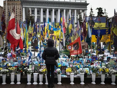 Seorang warga setempat berdiri di depan tugu peringatan sementara untuk tentara Ukraina di Lapangan Kemerdekaan, Kyiv, saat peringatan keempat invasi Rusia ke Ukraina, Selasa 24 Februari 2026. Hari ini, perang Rusia-Ukraina yang pecah pada 24 Februari 2022 telah berlangsung selama empat tahun. (HENRY NICHOLLS/AFP)