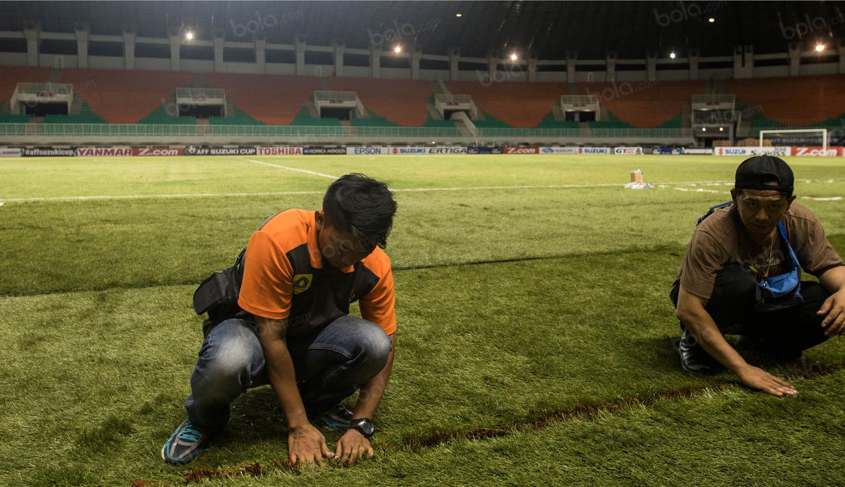 Pekerja merapihkan rumbut sintetis saat persiapan jelang laga semifinal Piala AFF 2016 antara Timnas Indonesia melawan Vietnam di Stadion Pakansari, Jawa Barat, Jumat (3/12/2016). (Bola.com/Vitalis Yogi Trisna)
