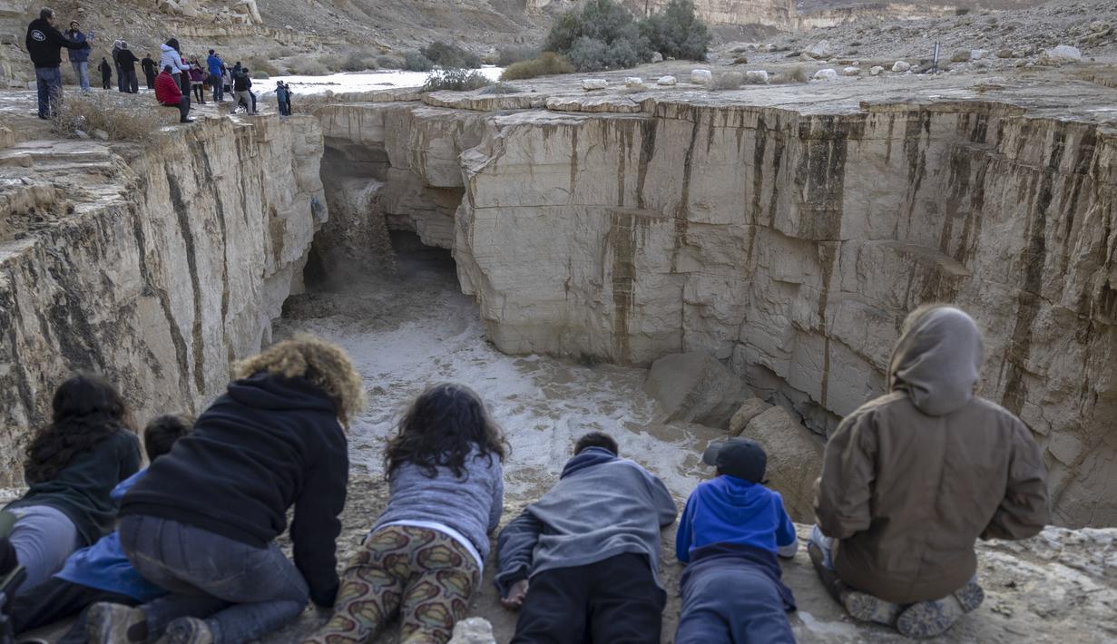 Warga Israel menyaksikan banjir bandang terjadi menyusul hujan lebat di gurun Negev di sebelah timur kota Dimona Israel pada 26 Desember 2022. Hujan lebat mengguyur Israel pada hari Senin (26/12) membanjiri jalan-jalan kota, memicu banjir bandang di dasar sungai gurun yang kering dan membasahi daerah pedesaan karena suhu turun ke level terendah musim ini. (AFP/Menahem Kahana)