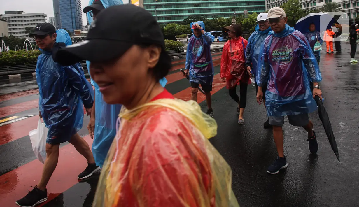 Warga dengan menggunakan jas hujan berolahraga di tengah rintik hujan pada Car Free Day atau hari bebas kendaraan di kawasan Bundaran Hotel Indonesia (HI), Jakarta, Minggu (12/2/2023). Hujan yang mengguyur Ibu Kota sejak malam sampai pagi ini tak menyurutkan semangat warga untuk tetap berolahraga di area CFD. (Liputan6.com/Johan Tallo)