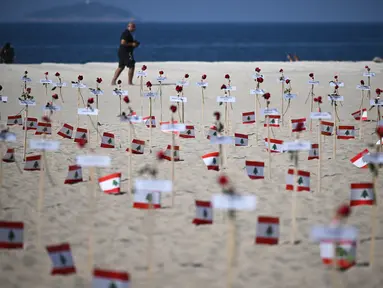 Seorang pria berjalan melewati 245 mawar yang ditempatkan oleh LSM Rio da Paz beserta nama korban dan bendera Lebanon untuk memperingati 3 tahun sejak ledakan Beirut 2020 di Pantai Copacabana, Rio de Janeiro, Brasil, diambil pada 4 Agustus 2023. (AFP/Carl De Souza)