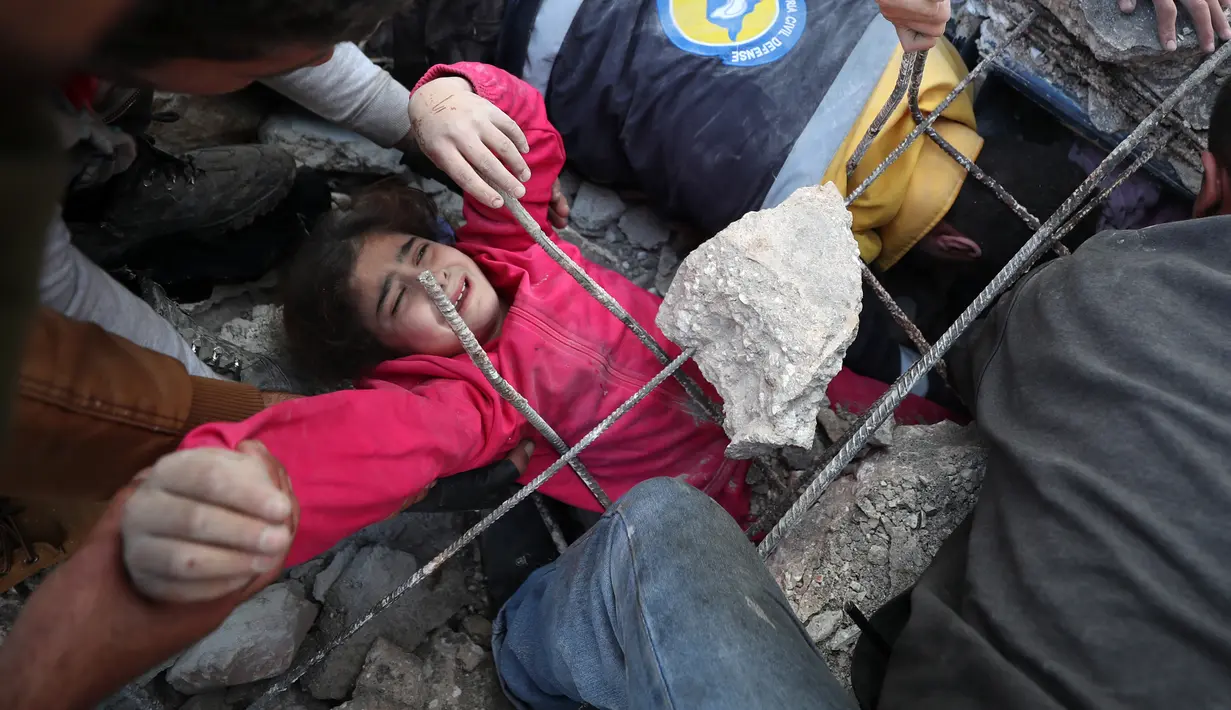 Seorang gadis menangis saat anggota Syrian Civil Defence atau White Helmets berusaha menyelamatkannya dari timbunan puing bangunan usai serangan udara pasukan pemerintah di Desa Tal Mardikh, Provinsi Idlib, Suriah, Kamis (19/12/2019). Pasukan Suriah kian intens menyerang Idlib. (Omar HAJ KADOUR/AFP)