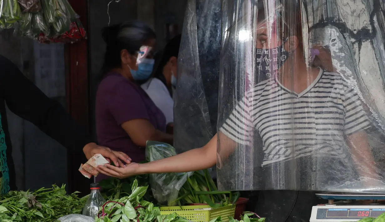 Penjual sayuran menerima pembayaran dari balik tirai plastik untuk mencegah virus corona di sebuah pasar di kota Quezon, Filipina, Selasa (22/9/2020). Presiden Rodrigo Duterte mengatakan telah memperpanjang status masa darurat Covid-19 di negaranya hingga satu tahun ke depan. (AP Photo/Aaron Favila)
