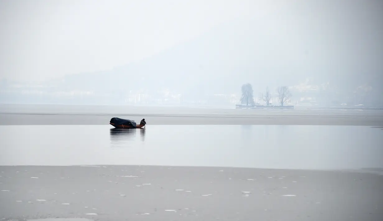 Seorang nelayan beraktivitas di danau Dal yang beku di Srinagar, Kashmir yang dikuasai India (7/1). Musim salju telah mengakibatkan gangguan lalu lintas udara dan lalu lintas jalan antara Srinagar dan Jammu. (AFP Photo/Tauseef Mustafa)