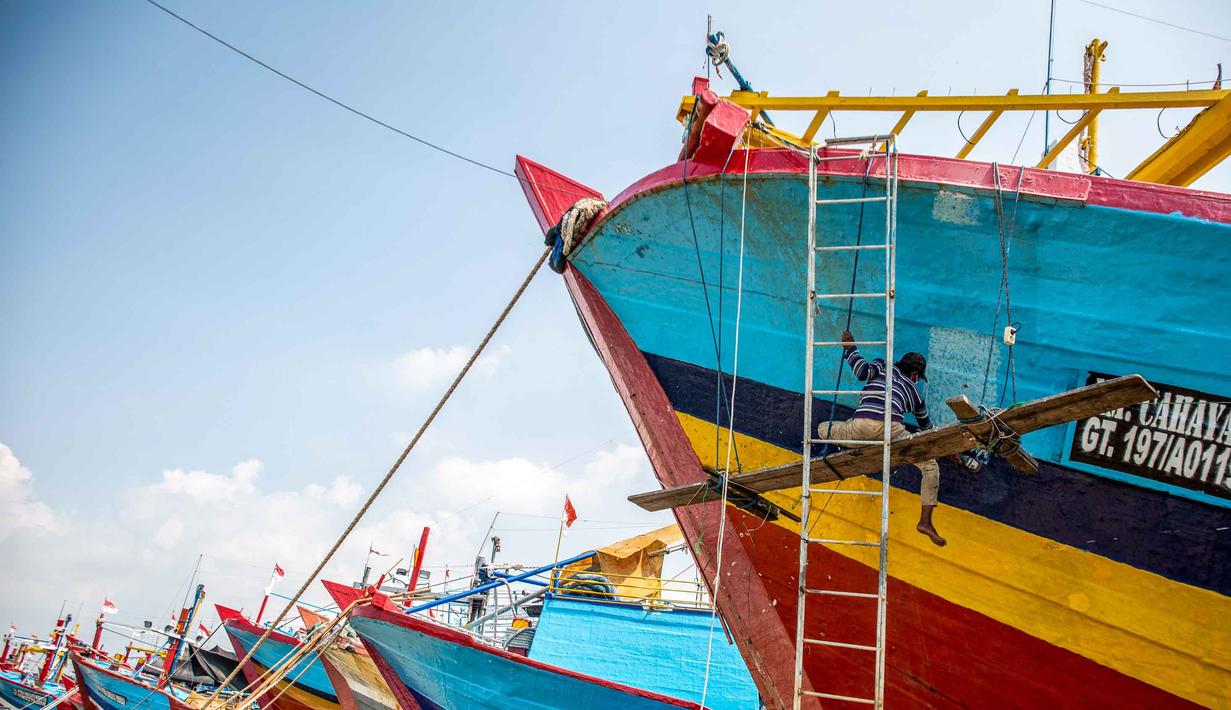 Berhentinya ribuan kapal berdampak pada sepinya aktivitas perdagangan di Tempat Pelelangan Ikan (TPI). Tampak dalam foto, seorang pria mengecat ulang perahu nelayan sementara kapal-kapal lain tetap berlabuh di Pelabuhan Juwana, Jawa Tengah, Rabu 6 Mei 2026. (Devi RAHMAN/AFP)
