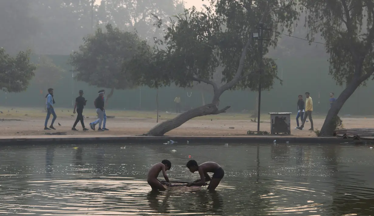Anak-anak mandi di air kolam hias dekoratif yang menghiasi taman-taman yang mengelilingi monumen Gerbang India di tengah kondisi kabut asap tebal di New Delhi (30/10). (AFP Photo/Dominique Faget)