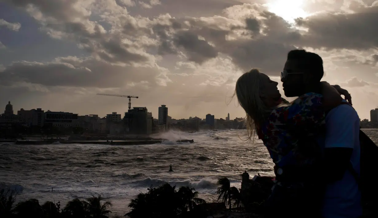 Suami istri berpelukan saaat ombak besar terlihat di laut Malecon di Havana, Kuba (21/12). Letak kota yang berdiri pada tahun 1515 ini relatif strategis. (AP Photo / Ramon Espinosa)