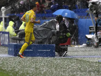 Pemain Ukraina, Yevhen Konoplyanka (kiri) berlari menghindari terjangan hujan batu es saat melawan Irlandia Utara  pada laga grup C  Euro 2016 di Stadion Parc Olympique Lyon, Kamis ( 16/6/2016) WIB. AFP/Philppe Desmazes)