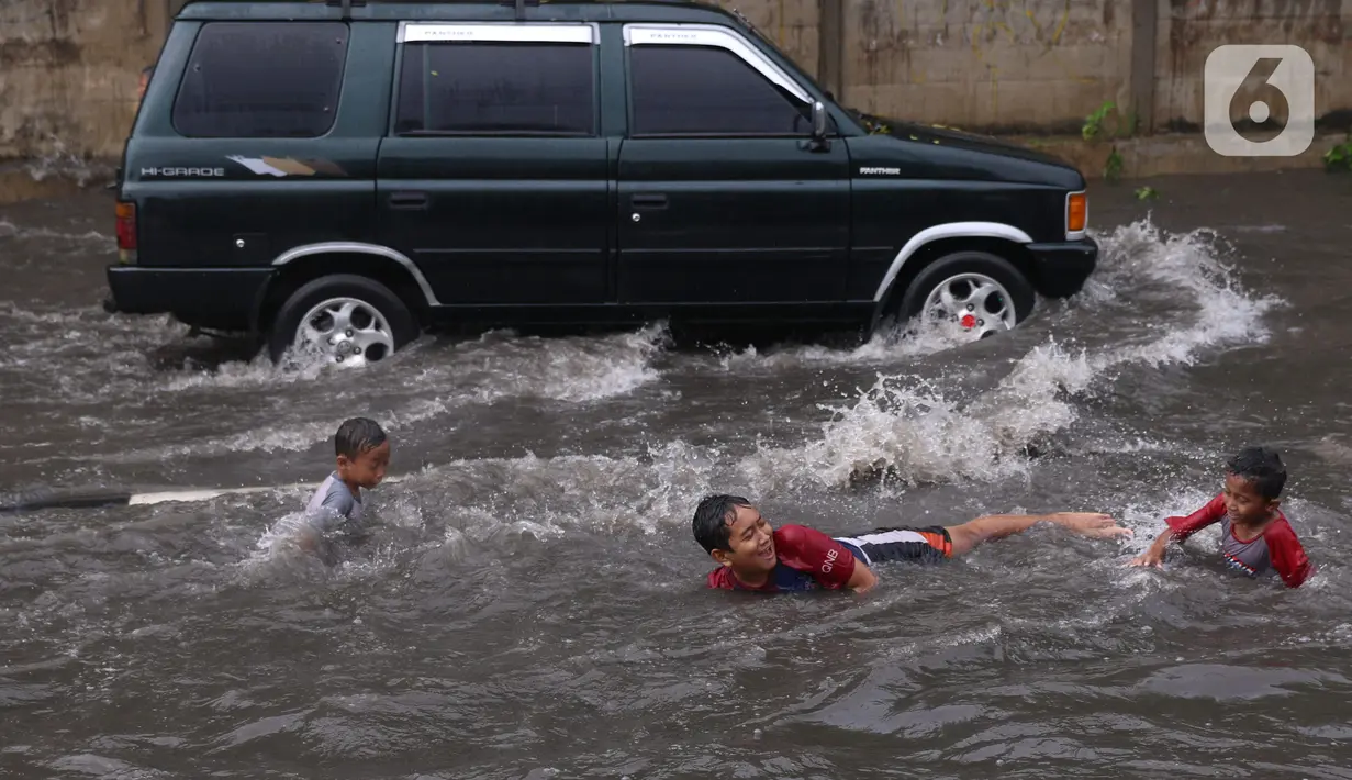 Sejumlah anak bermain banjir saat melanda jalan Bayangkara Pusdiklat, Kota Tangerang Selatan, Banten, Selasa (2/11/2021). Aksi anak anak tersebut dapat membahayakan keselamatan jiwa karena banyaknya kendaraan yang melintas menerjang banjir. (Liputan6.com/Angga Yuniar)