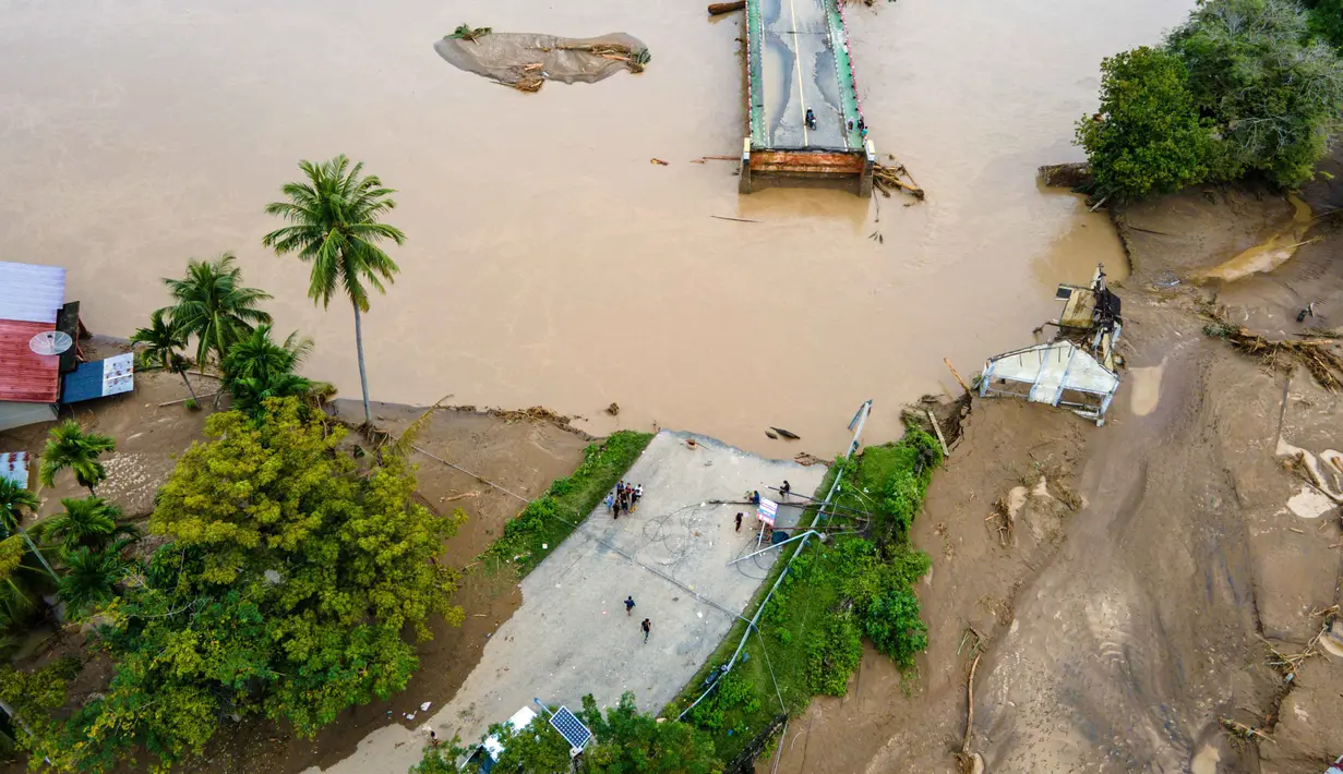 Sebagian badan jembatan ambruk dan terputus membuat arus lalu lintas lumpuh total. Tampak foto udara menunjukkan jembatan yang rusak akibat banjir bandang di jalan utama yang menghubungkan Aceh dan Sumatera Utara di Meureudu, Kabupaten Pidie Jaya, Provinsi Aceh, pada Jumat 28 November 2025. (CHAIDEER MAHYUDDIN/AFP)