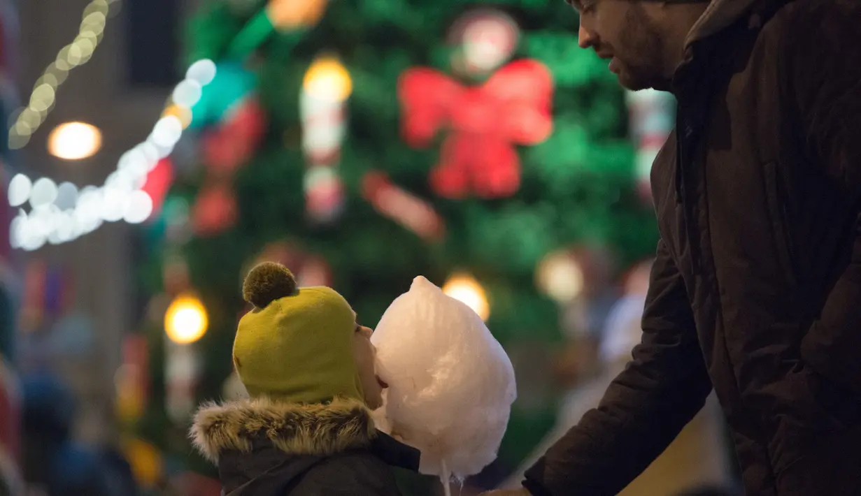 Seorang anak menyantap permen kapas di pasar Natal di St. Petersburg (20/12/2020). Wisatawan juga dapat mengunjungi konser dadakan, roti jahe, mainan, gua, dan wahana pasar malam. (Xinhua/Irina Motina)