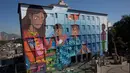 Mural berjudul 'Contos' yang dilukis oleh seniman Brasil, Luna Buschinelli, di dinding gedung sekolah Rio de Janeiro, (19/6). Mural tersebut mengisahkan seorang ibu buta huruf yang sedang membacakan buku cerita kepada anak-anaknya. (AP/Silvia Izquierdo)